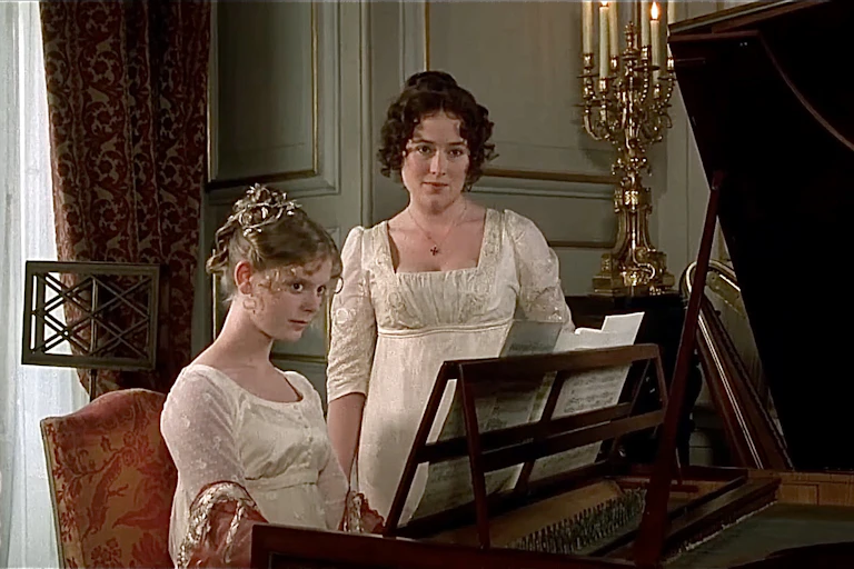 a young woman sits at a piano, with another young woman standing beside her