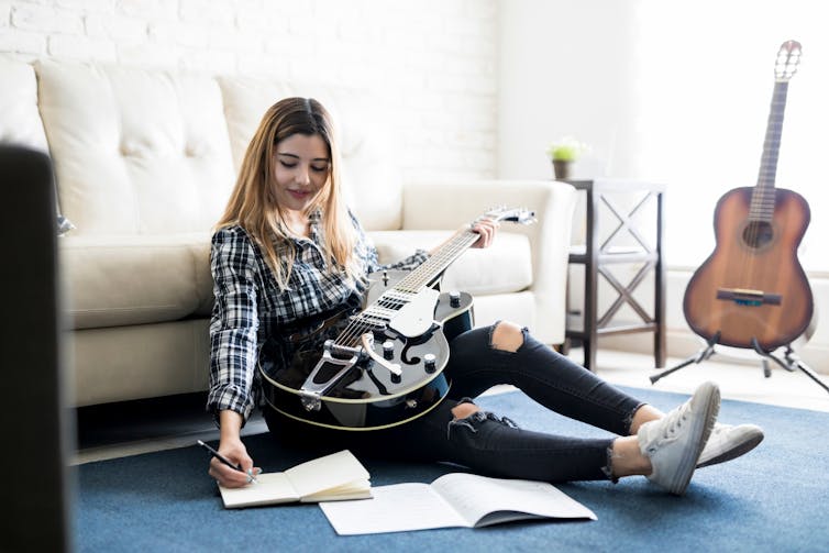 A girl sitting on the floor with a guitar and notebooks