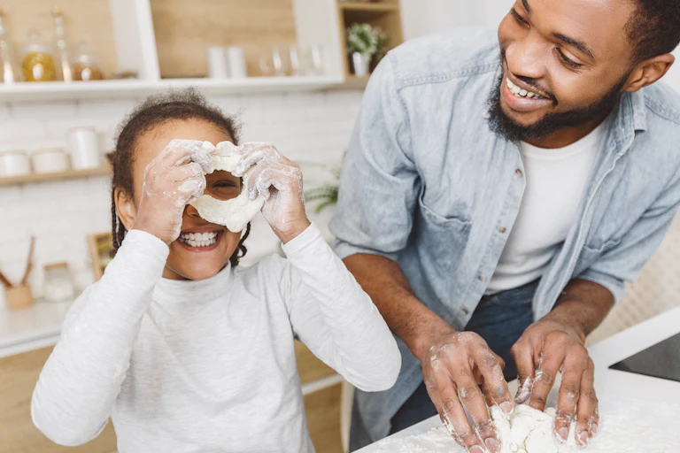A girl peeks through a circle of doughs she's making with her father.