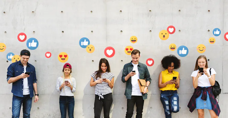 Six young people leaning against a concrete wall, all watching their mobile phones. Emoji icons are emanating from the screens.