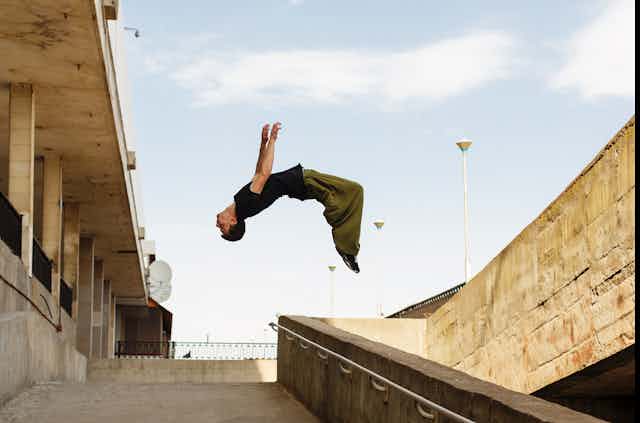 A young man doing a backflip in the air above a concrete stairwell.