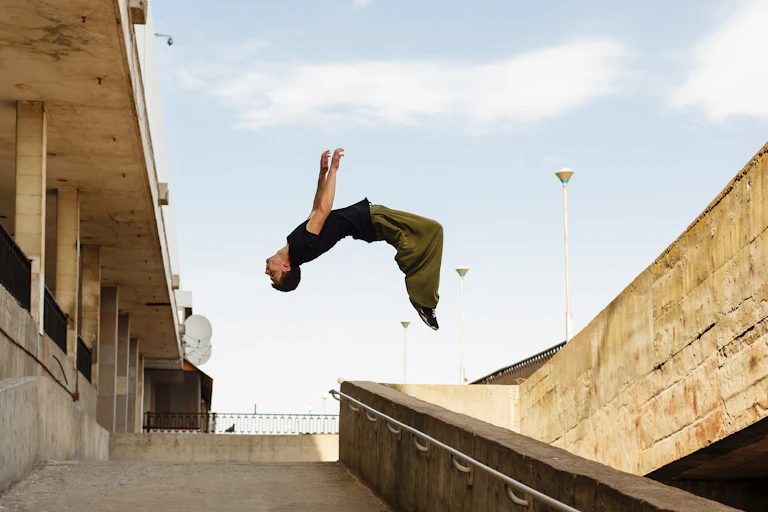 A young man doing a backflip in the air above a concrete stairwell.