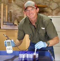 A researcher holding a gauge samples vials of fluid.