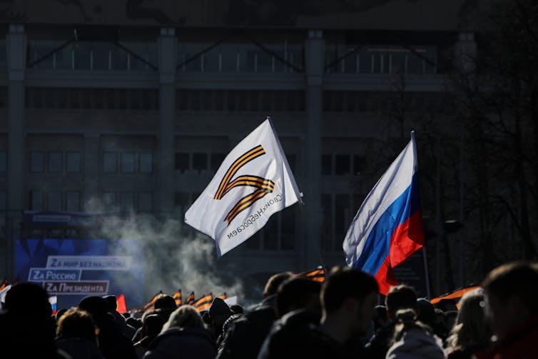 Two flags - one with the letter Z, one Russian - stand above people's heads during a concert.