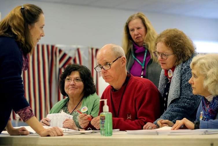 People on one side of a table, listening to a woman talking to them from the other side.