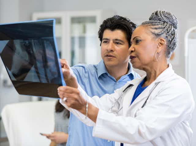 woman in white coat points something out on X-ray to a man