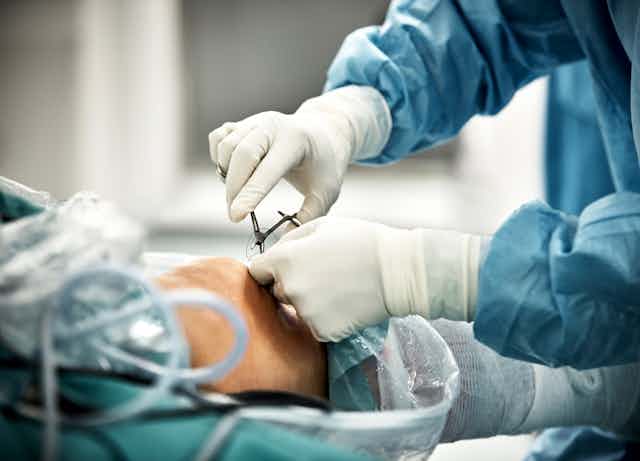 A surgeon's gloved hands are holding medical scissors while sewing up a patient