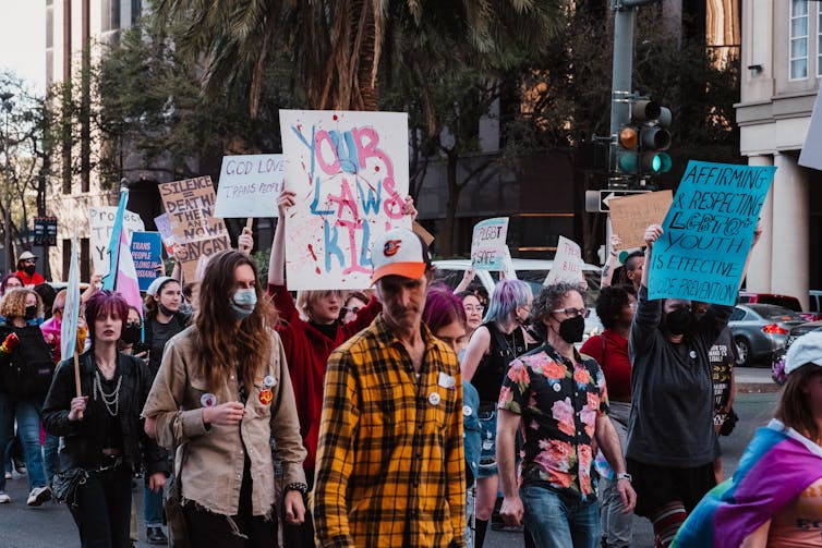 People march holding signs like 'your laws kill' and 'god loves trans people'