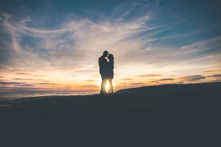 embracing couple silhouetted against sunset