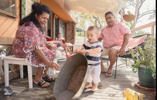 An Aboriginal family are sitting together playing with their infant child.
