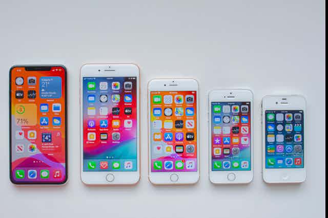 Several models of the iPhone are in a line, with the home screen open