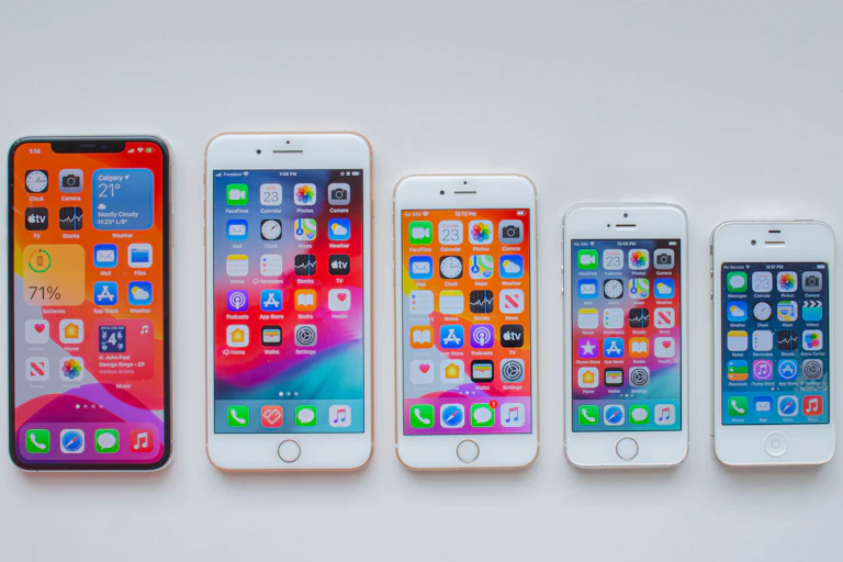 Several models of the iPhone are in a line, with the home screen open