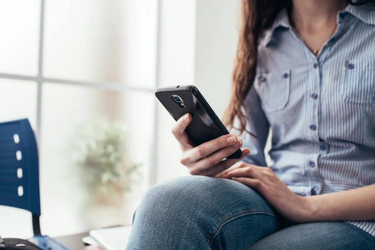 Photo of a woman sitting in a waiting room looking at her phone.