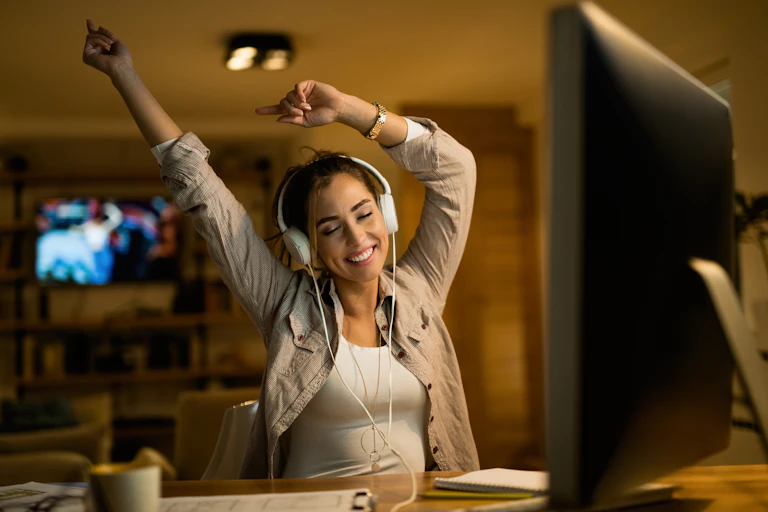 Female student sitting at her desk smiles and stretches as she listens to music