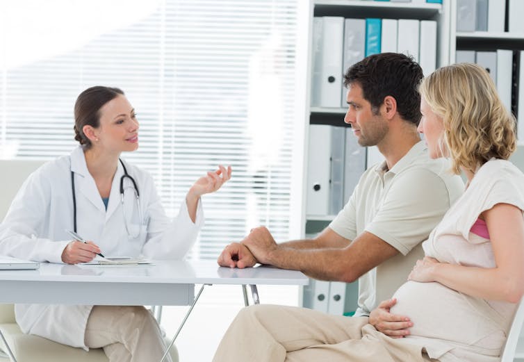 Expectant couple speak with female doctor in doctor's office.