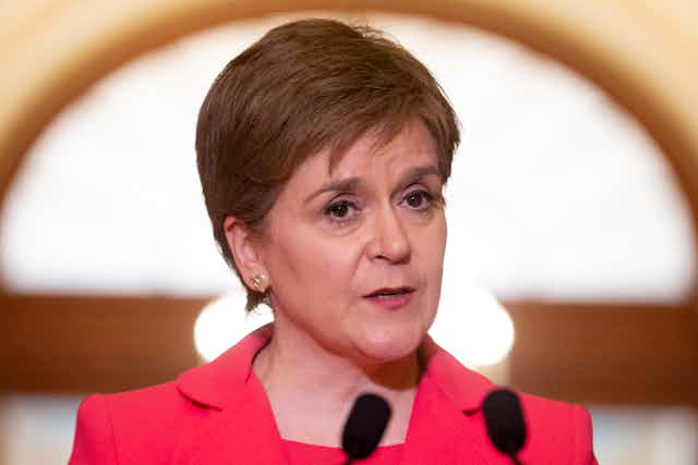 Close-up photo of First Minister Nicola Sturgeon in a bright pink suit speaking at a podium