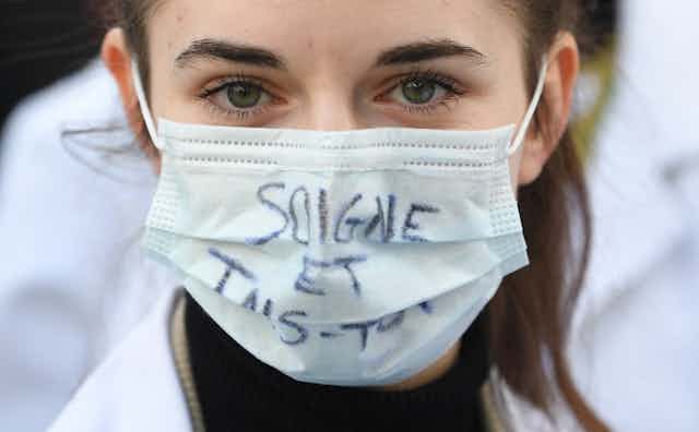 Une jeune étudiante en médecine porte un masque où est écrit « Soigne et tais-toi »