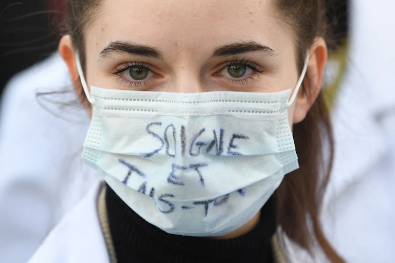 Une jeune étudiante en médecine porte un masque où est écrit « Soigne et tais-toi »