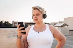 Woman in workout clothes and headphones looking at a smartphone