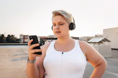 Woman in workout clothes and headphones looking at a smartphone