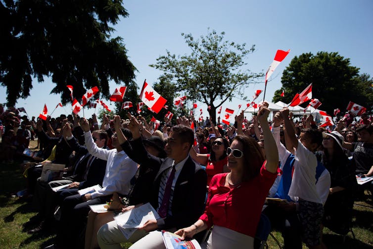 Canadian residents of Iran who have just received their citizenship are waving Canadian flags after the citizenship oath ceremony in Vancouver, BC, in July 2017