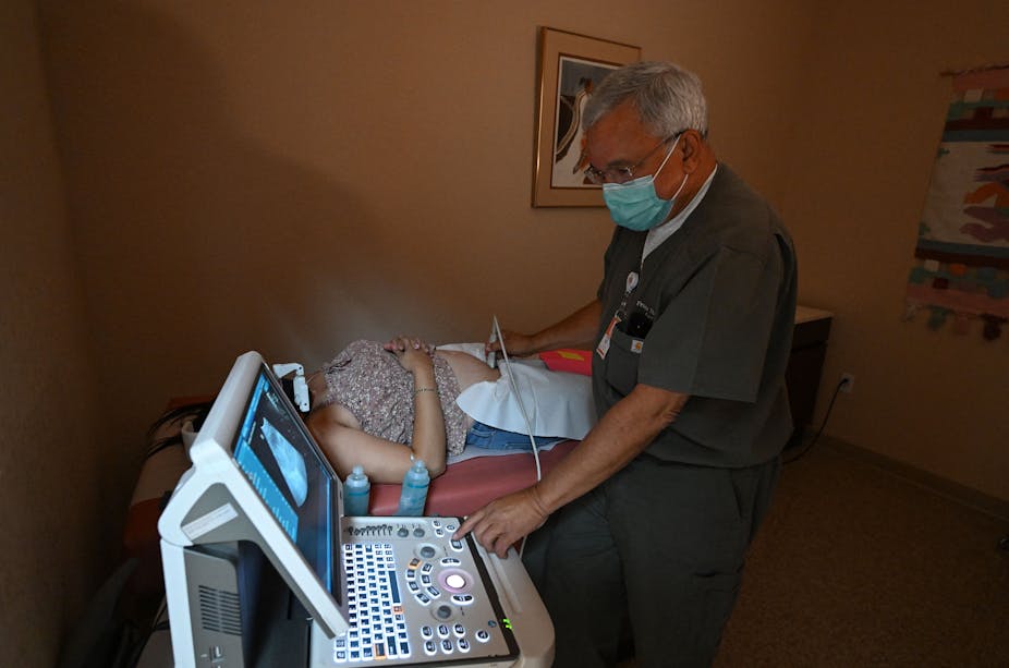 A man performing a sonogram on a woman who is lying down.