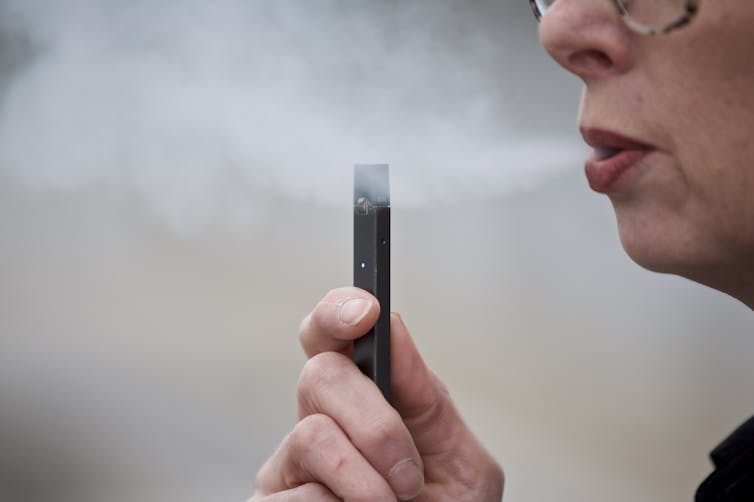 A woman exhaling a cloud of vapor while holding a Juul e-cigarette.