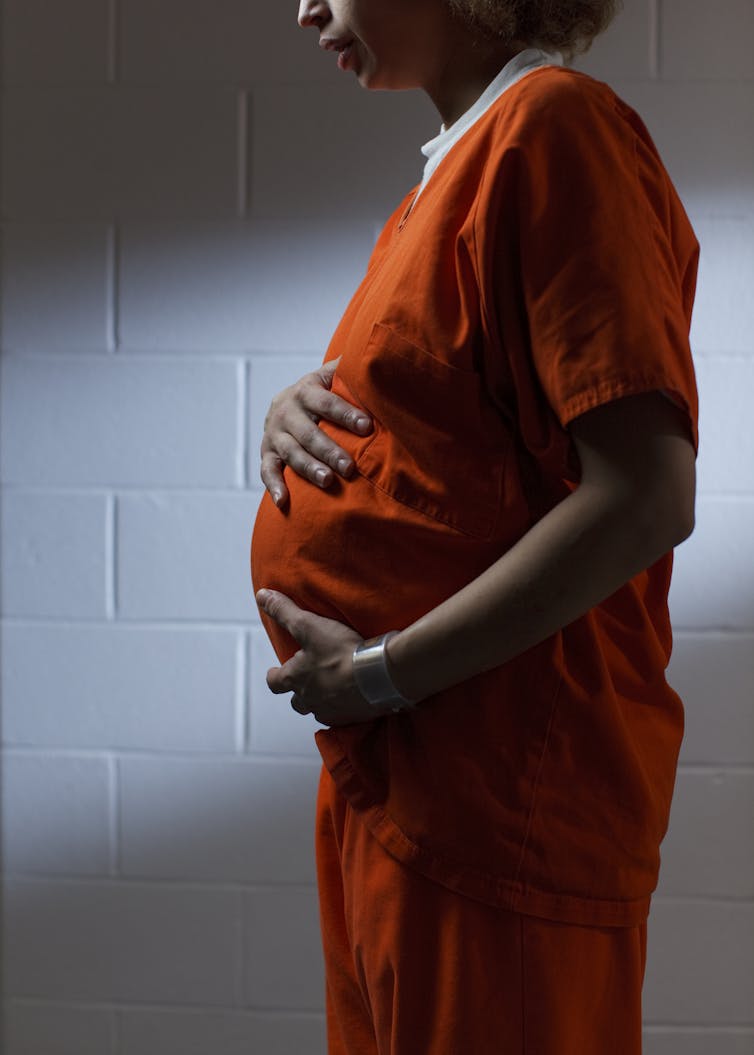 A pregnant woman in orange stands in a profile shot, holding her belly