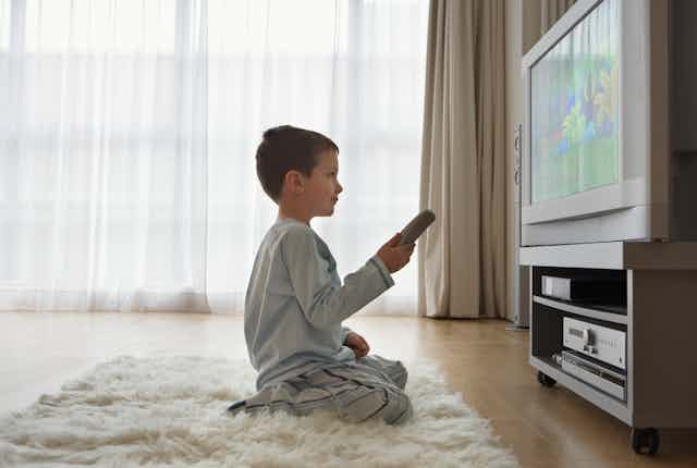 A young boy, with a remote control unit in hand, watches television in his living room.