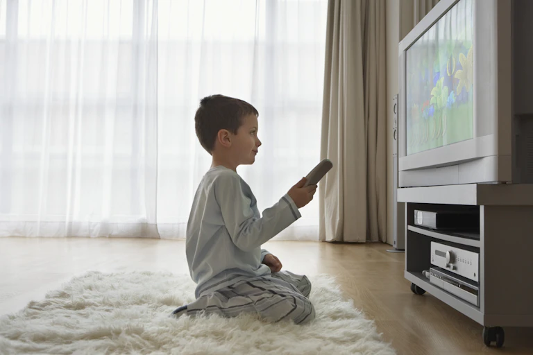 A young boy, with a remote control unit in hand, watches television in his living room.