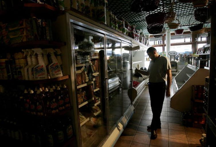 A man stands in front of a dark freezer case packed with pizzas and other frozen meals.