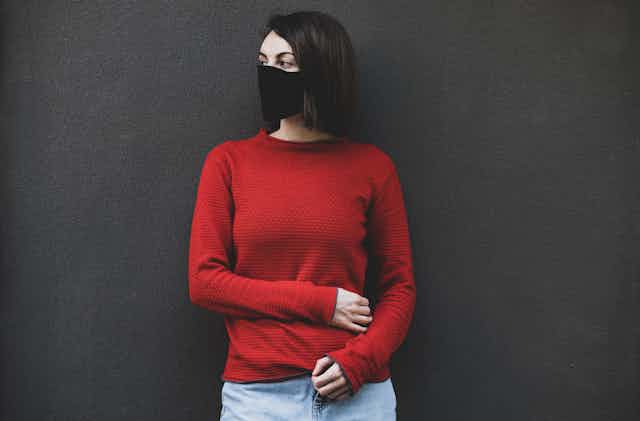 Woman in a red jumper and black mask looks to her side
