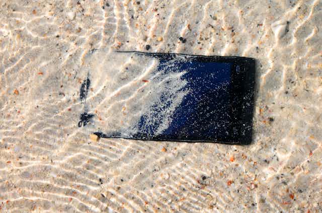 Phone is dropped underwater, partially covered by sand