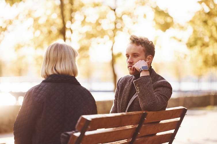 Man and woman sit on a park bench talking