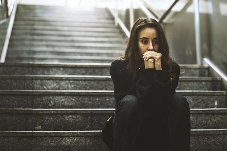 A worried woman is sitting on a set of stairs outdoors.