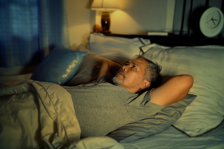 A middle aged man lies awake in bed looking worried.