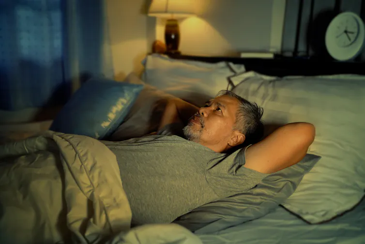 A middle aged man lies awake in bed looking worried.