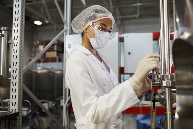 A person wearing protective equipment and a white coat turns a metal wheel