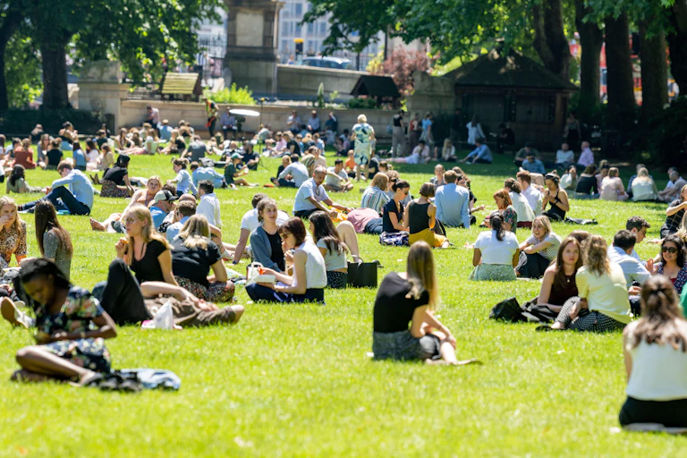 People sitting outdoors in a park in London on a sunny day.