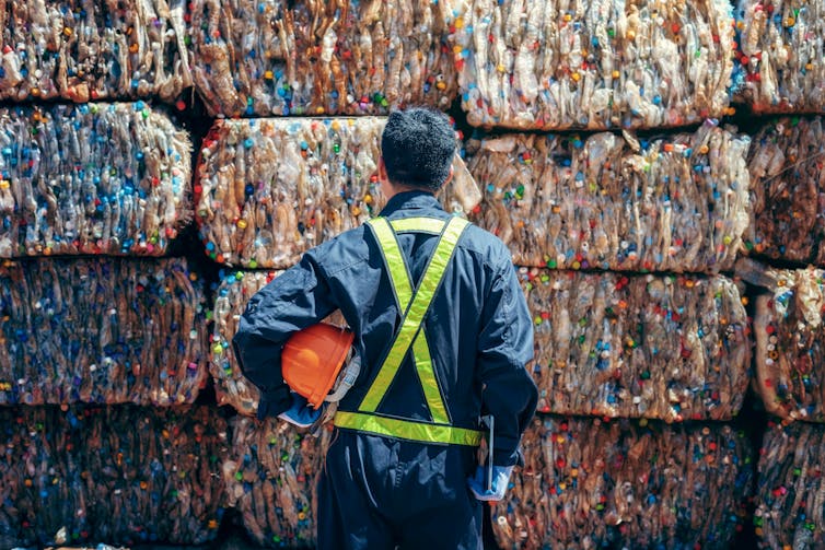 A person stands looking at cuboids of crushed plastic bottles