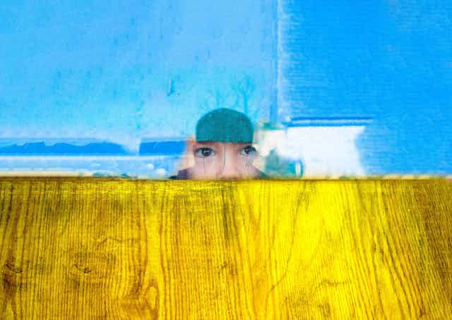 A child looking out of a broken window amid colours reminiscent of the Ukrainian flag.