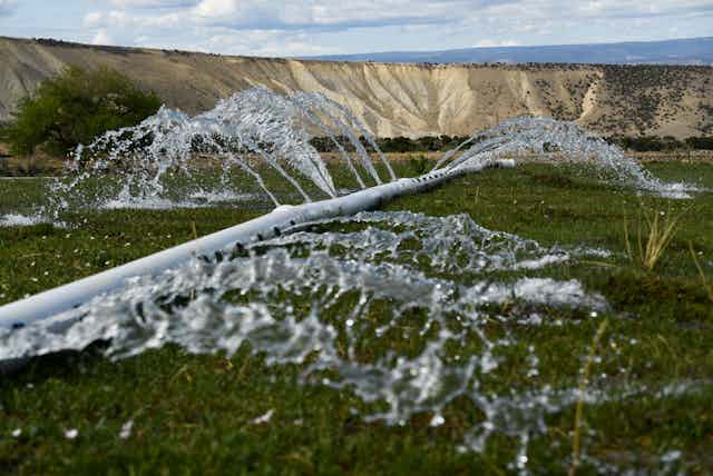 Water sprays onto a field from holes in a metal pipe