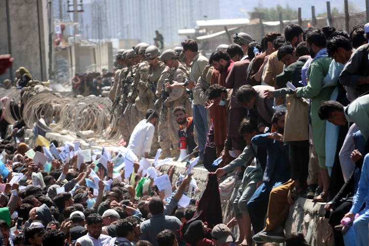 Crowds of people waving their papers at officials in an attempt to be rescued from Kabul airport.