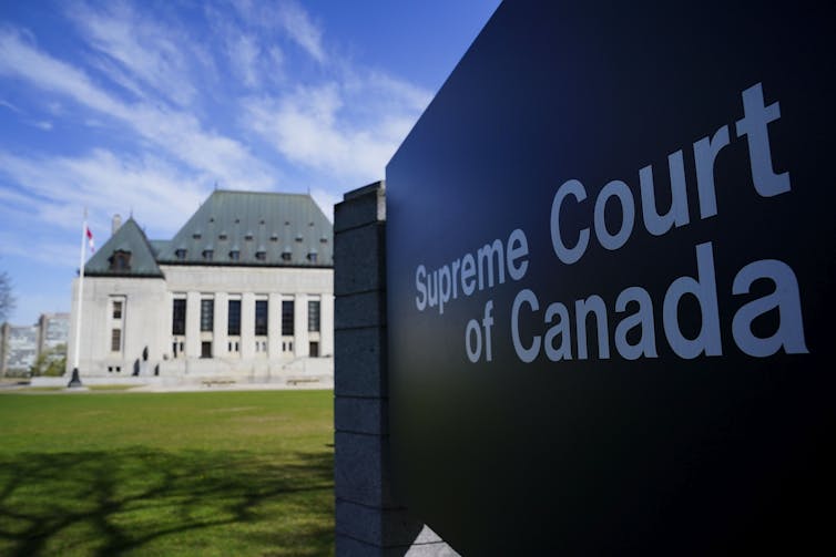 A sign that reads Supreme Court of Canada with the Supreme Court in the background under blue skies.