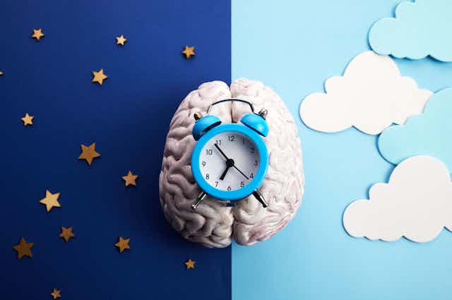 Alarm clock lying on top of a brain, with a background of a starry night sky on one half and a cloudy day on the other