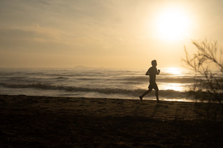 Silhouette of person running by the sea at sunrise