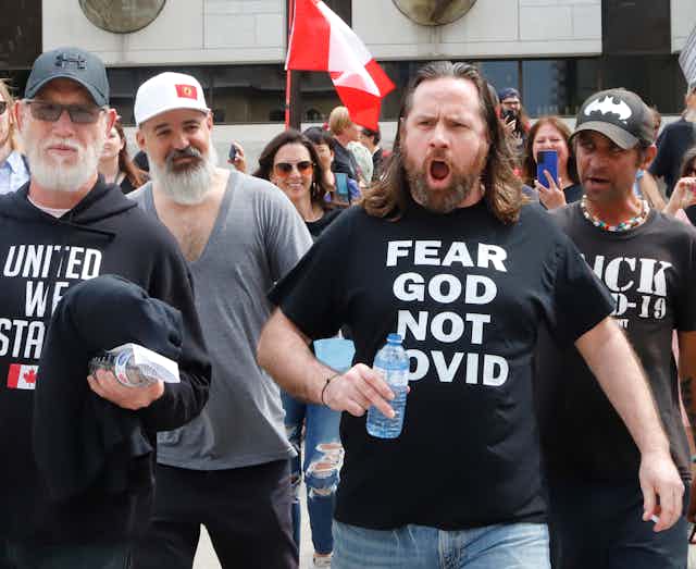 A bearded man bellows wearing a Fear God Not Covid black T-shirt.