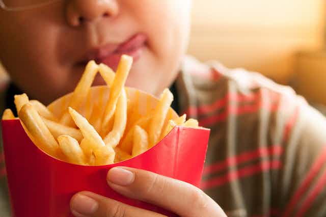 A young boy holds a red open container filled with french fries.