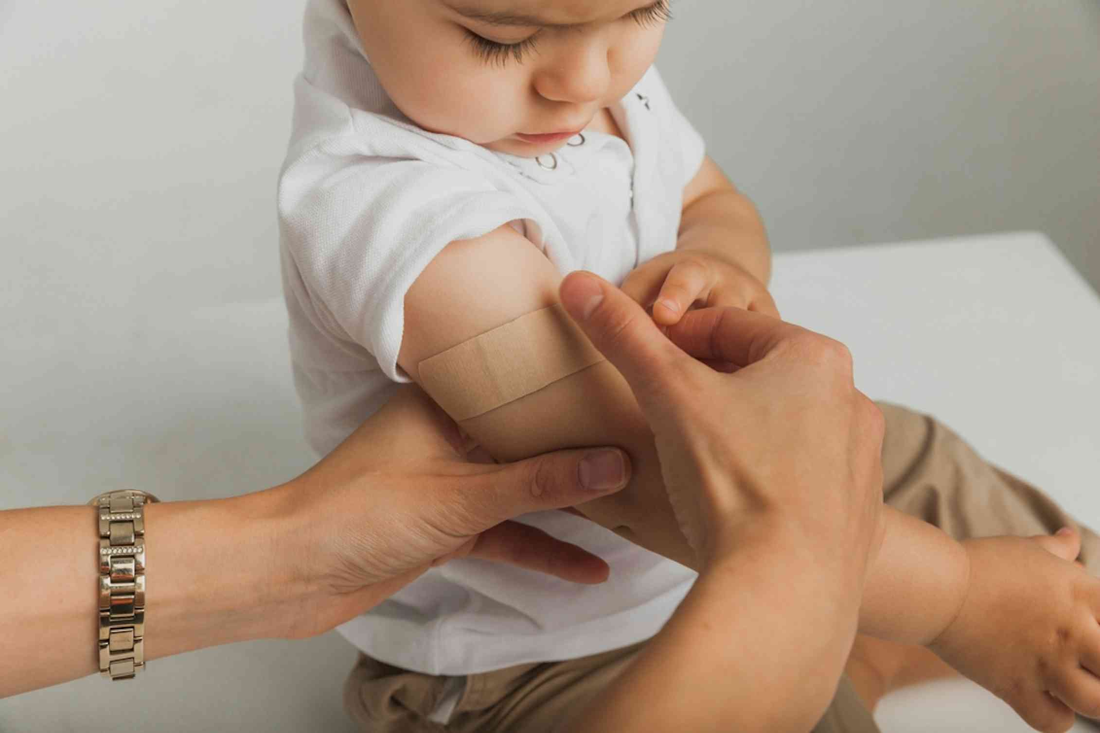 Health worker putting on bandaid on upper arm of young child after vaccination