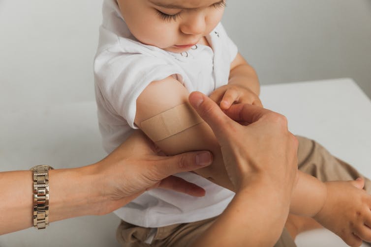 Health worker putting on bandaid on upper arm of young child after vaccination